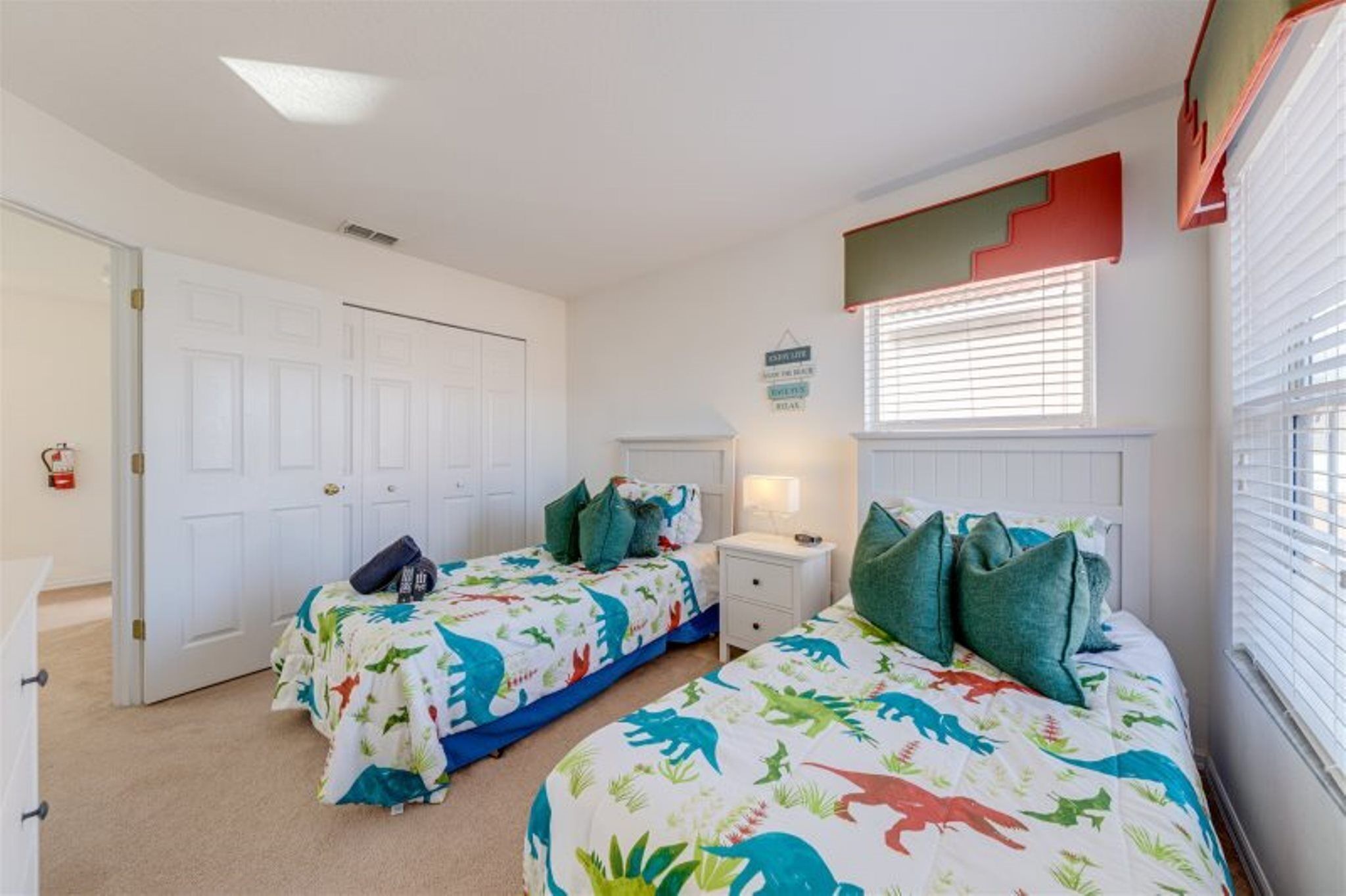A bedroom with two beds, a white door, a nightstand, and a window with blinds.