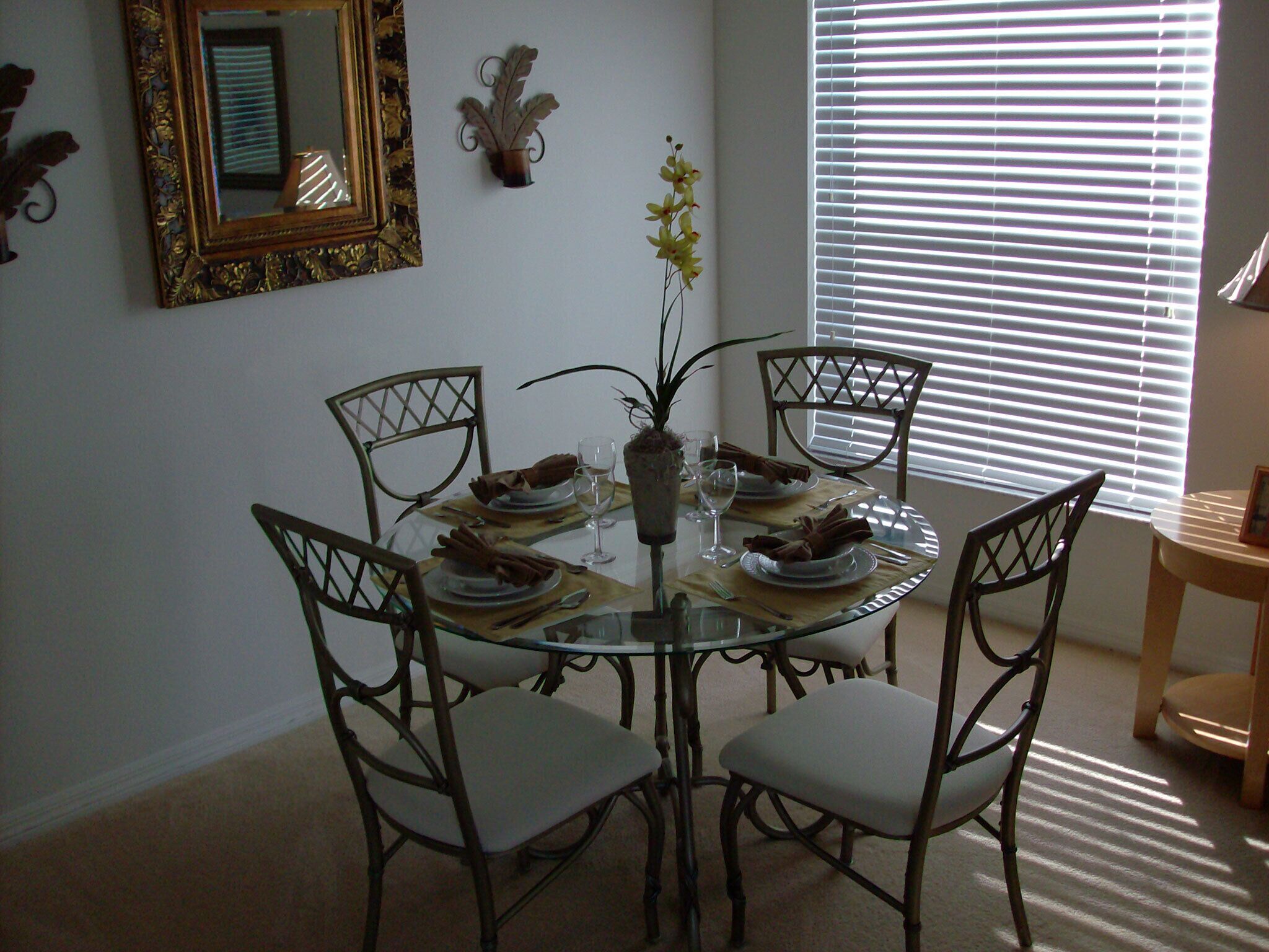 A dining area with a round glass table, six chairs, and a vase with flowers.