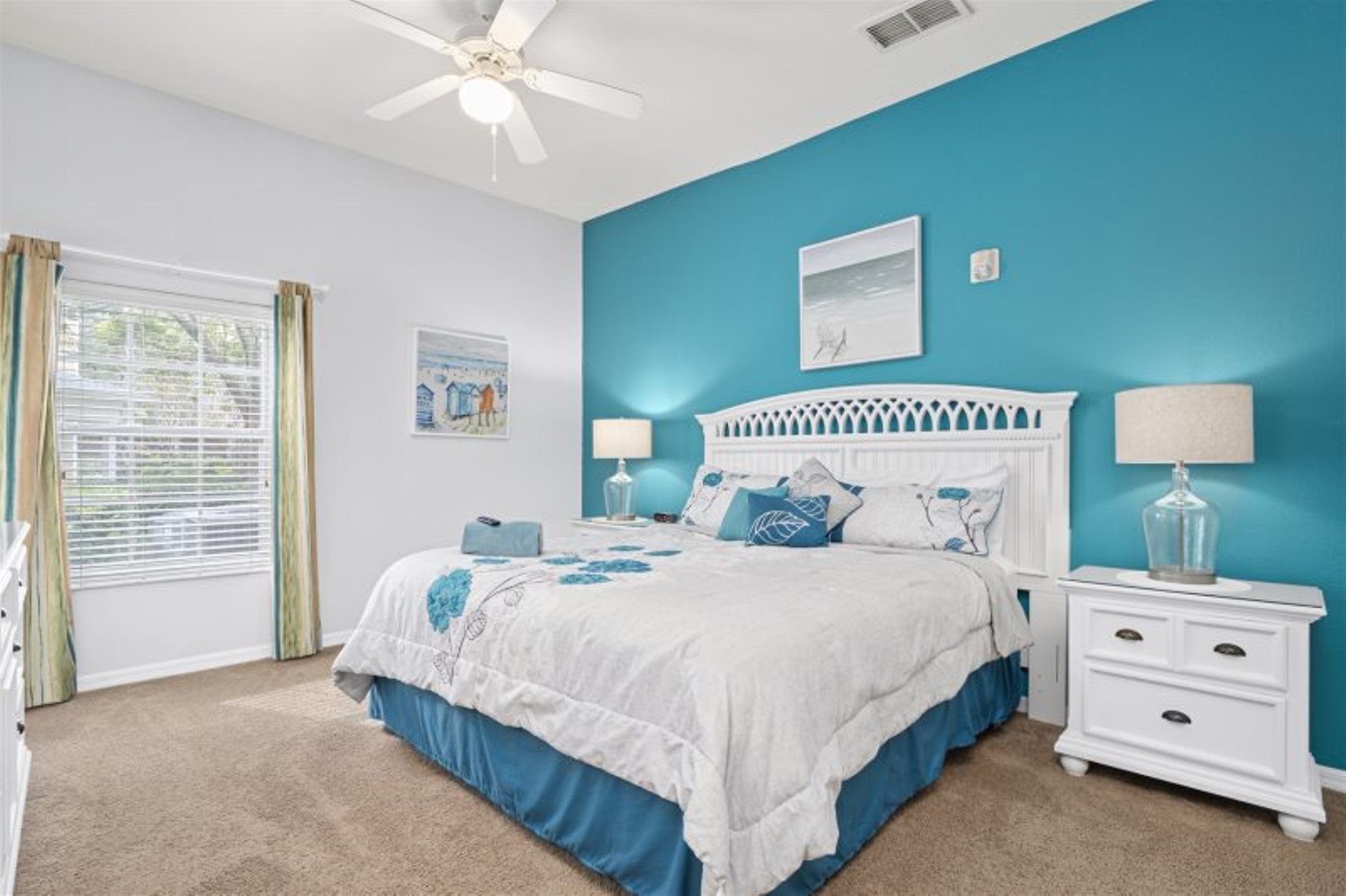A bedroom with a bed, nightstands, a ceiling fan, and a window with curtains.