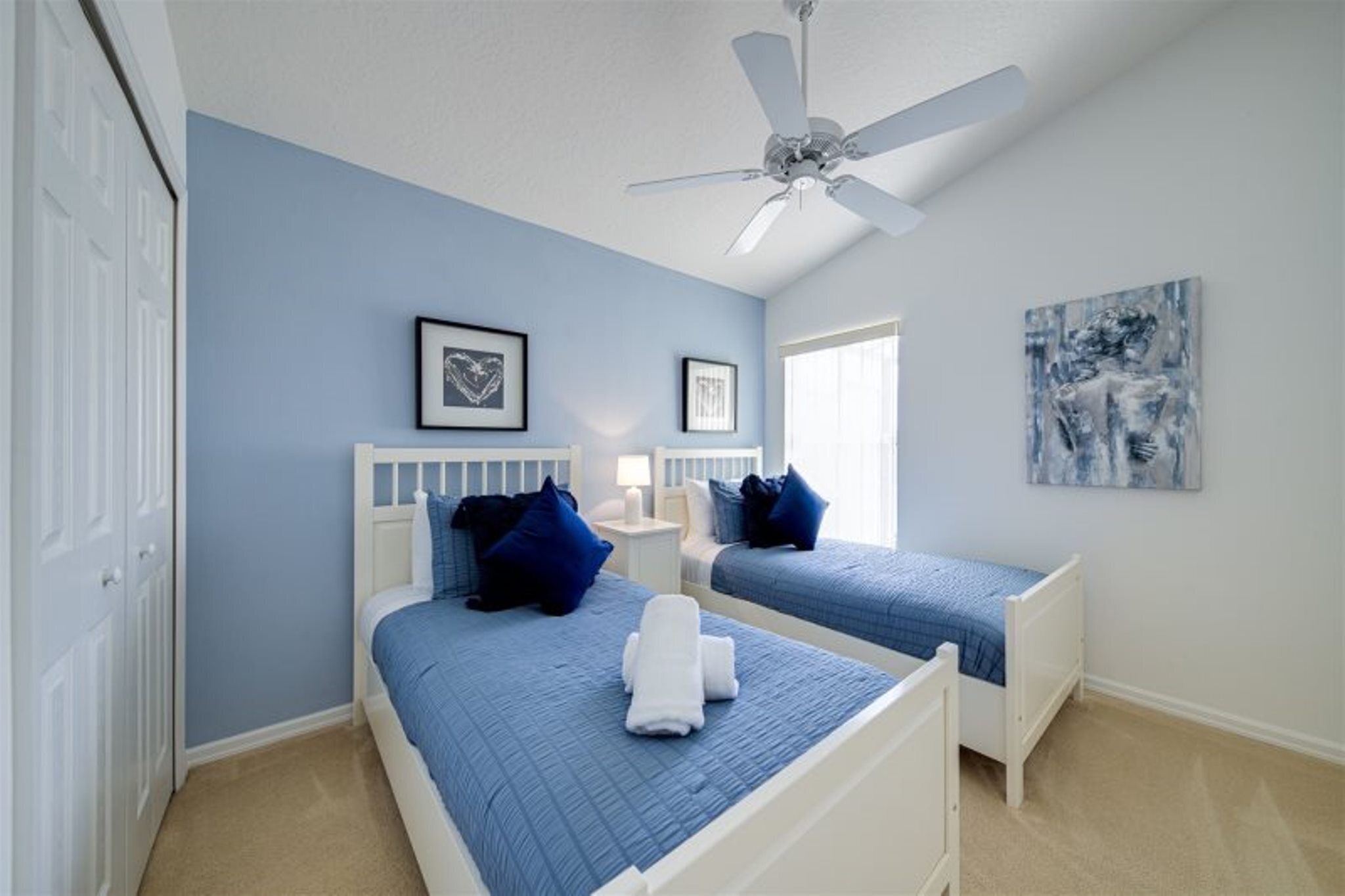 A bedroom with two beds, a ceiling fan, and artwork on the walls.