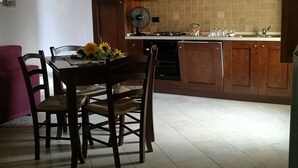Een keuken met houten kasten, een eettafel met stoelen, een ventilator en een vaas met bloemen.