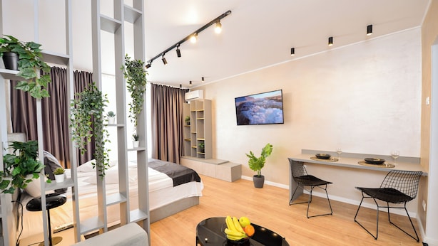 A modern, well-lit living room with a sofa, a dining table with chairs, a TV mounted on the wall, and potted plants. - Park Studio Cismigiu Gardens - Quiet Room - Smart Tv (Bucharest)