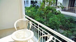 A balcony with a white wicker table and chairs, surrounded by a white railing, overlooking a lush green garden. - Spacious 3rd Floor Studio at Baan Suan Lalana (Pattaya)