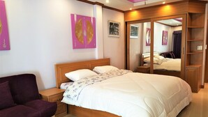 A bedroom with a large bed, a wooden nightstand, a purple sofa, and a wardrobe with a mirror. - Spacious 3rd Floor Studio at Baan Suan Lalana (Pattaya)