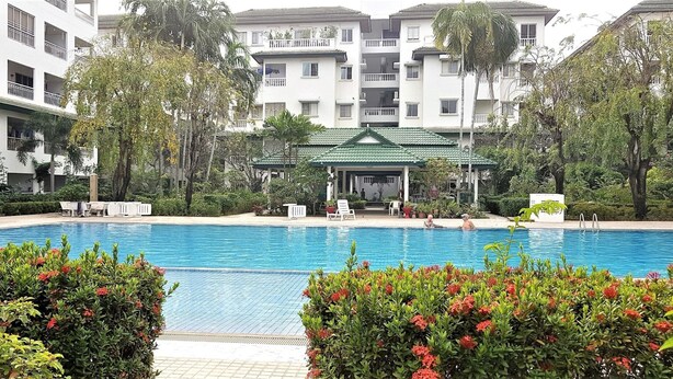 A swimming pool surrounded by lush greenery and a multi-story building with balconies. - Spacious 3rd Floor Studio at Baan Suan Lalana (Pattaya)