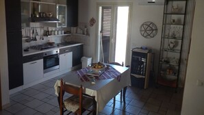 A compact kitchen with a dining area, featuring a table with chairs, a small refrigerator, and a shelf with decorative items. - A Relaxing Holiday, Even With Your Four-legged Friends (Avola)
