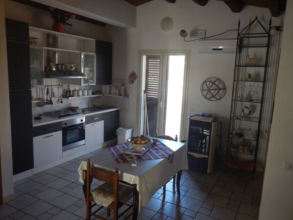 A compact kitchen with a dining area, featuring a table with chairs, a small refrigerator, and a shelf with decorative items. - A Relaxing Holiday, Even With Your Four-legged Friends (Avola)