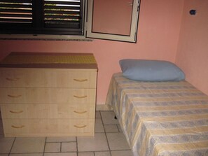 A bedroom with a wooden dresser, a bed with a patterned bedspread, a window with blinds, and a wall-mounted mirror. - A Relaxing Holiday, Even With Your Four-legged Friends (Avola)