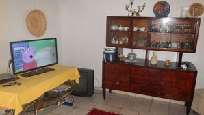 A living room with a television displaying a cartoon, a wooden cabinet with glass doors, and a red rug. - A Relaxing Holiday, Even With Your Four-legged Friends (Avola)