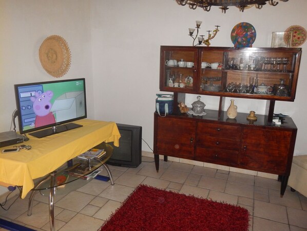 Una sala de estar con un televisor mostrando una caricatura, un mueble de madera con puertas de vidrio y una alfombra roja.