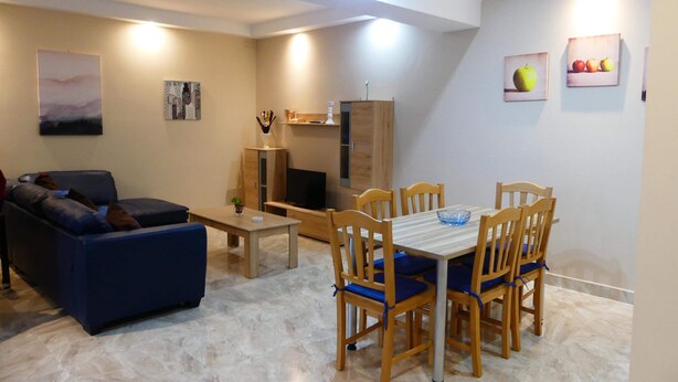 Un salon avec un canapé bleu, une table à manger en bois avec six chaises, un téléviseur et un meuble.