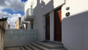 Un bâtiment blanc avec une porte en bois, un balcon et une entrée fermée par un portail.