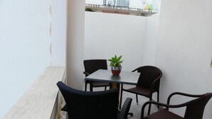 Un petit espace extérieur aménagé avec une table et quatre chaises, une plante en pot posée sur la table et un mur blanc en arrière-plan.