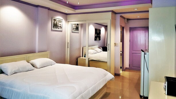 Une chambre d’hôtel avec un grand lit, un ventilateur de plafond, un miroir et une porte donnant sur une autre pièce.