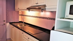 Une cuisine avec des meubles blancs, un plan de travail noir, un évier en acier inoxydable et un four à micro-ondes.