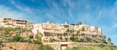 A multi-story hotel with balconies, located on a hillside with vegetation.
