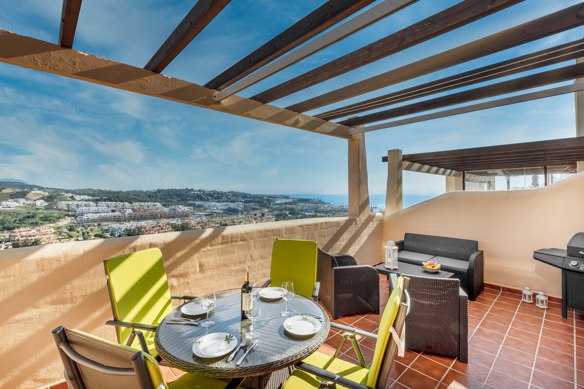 A terrace with a table set for dining, outdoor seating, and a view of a distant landscape.