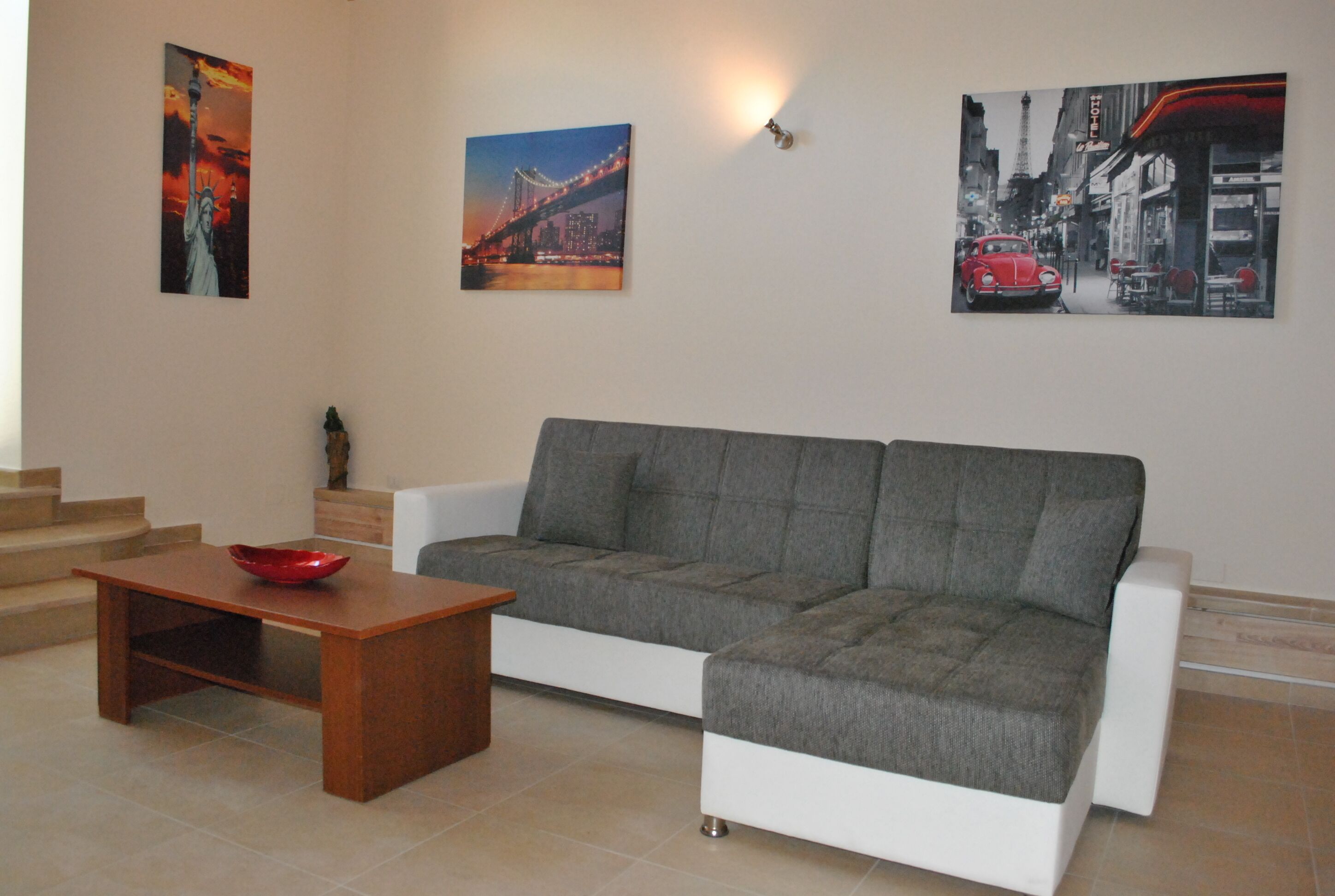 A living room with a grey sofa, a wooden coffee table, and a red bowl. There are stairs leading to an upper level.