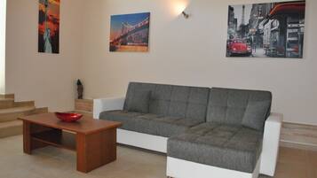 A living room with a grey sofa, a wooden coffee table, and a red bowl. There are stairs leading to an upper level.
