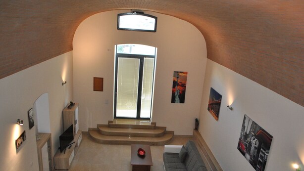 A spacious living area with a staircase leading to an upper floor, a television, and artwork on the walls. - Corona Matera Holiday Home (Matera)
