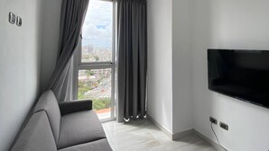 A modern living room with a grey sofa, a ceiling fan, a large window with curtains, and a flat-screen TV mounted on the wall. - Apartment Of 1 Bedroom Plus Study With Sofa Bed (Santo Domingo)