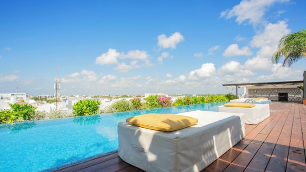 A rooftop infinity pool with wooden decking, white lounge chairs, and a view of the city skyline. - Lovely One Bedroom With Amazing Terrace View!! (Playa del Carmen)