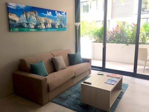A living room with a beige sofa, a coffee table, and a painting of cliffs. - Lovely One Bedroom With Amazing Terrace View!! (Playa del Carmen)