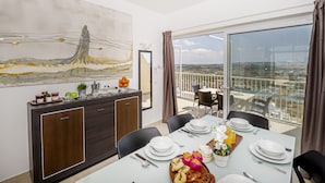 A dining area with a table set for four, a large abstract painting on the wall, and a view of the city through large windows. - Summer Breeze Penthouse With Hot Tub (Mellieha)