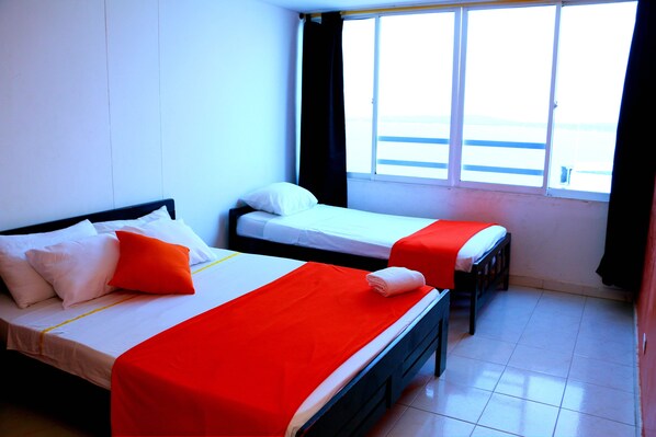 Une chambre d’hôtel avec deux lits, l’un recouvert d’une couverture rouge et l’autre d’une couverture blanche.