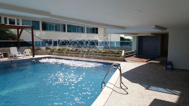 En swimmingpool med en fontän, omgiven av solstolar och en modern byggnad i bakgrunden.