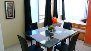 En matplats med ett glasbord och stolar, en liten växt som mittpunkt och en soffa med en orange kudde.