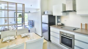 A modern kitchen with stainless steel appliances, a dining area with a table set for two, and a view through a glass partition to an outdoor area. - Cosy Studio Next to Cupecoy Beach for 4 pax (Lowlands)