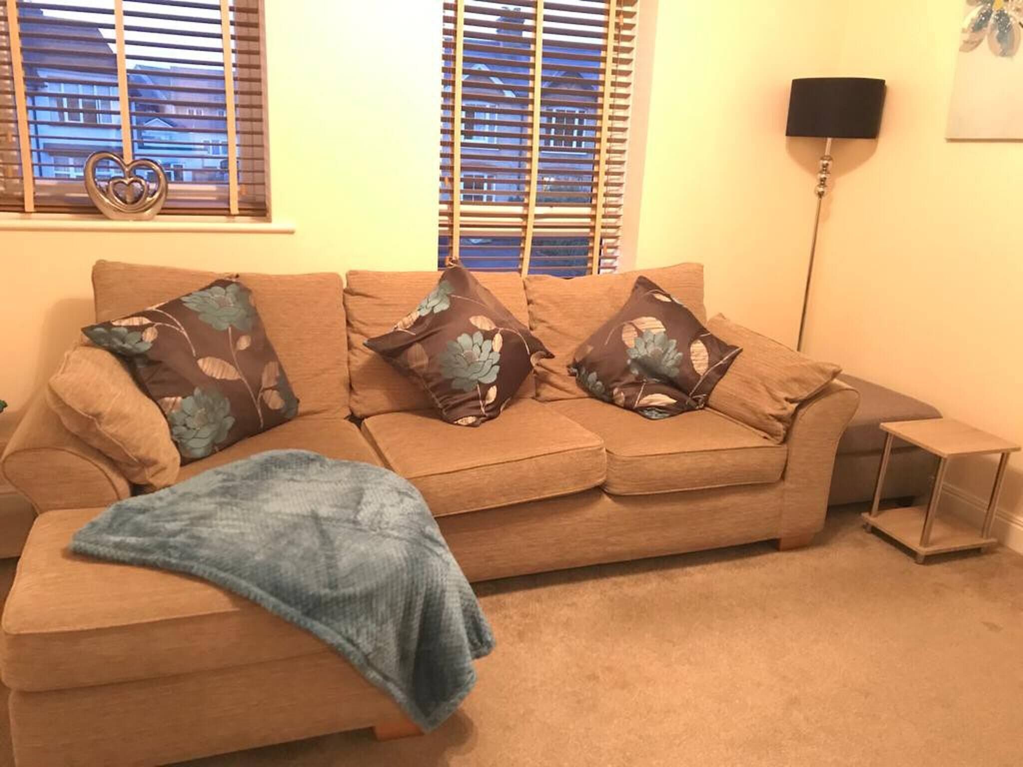 A living room with a beige sofa, three patterned throw pillows, a blue blanket, and a small side table.