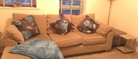 A living room with a beige sofa, three patterned throw pillows, a blue blanket, and a small side table.
