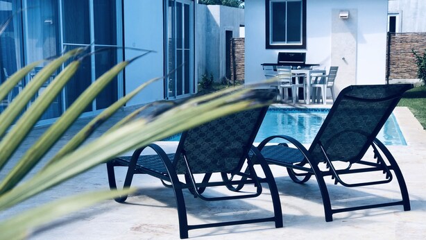 A modern outdoor pool area with two lounge chairs and a table, surrounded by a white building with large windows. - Sosua Ocean Vilage Villa With 2 Bedrooms And Privat Pool (Sosúa)