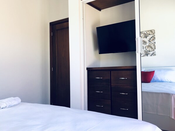 A bedroom with a bed, a wardrobe, a television, and a painting on the wall.