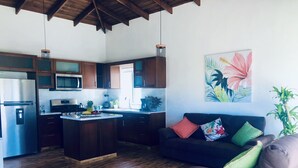 A modern kitchen with wooden cabinets, a central island, and a dining area with a dark-colored sofa and colorful cushions. - Sosua Ocean Vilage Villa With 2 Bedrooms And Privat Pool (Sosúa)
