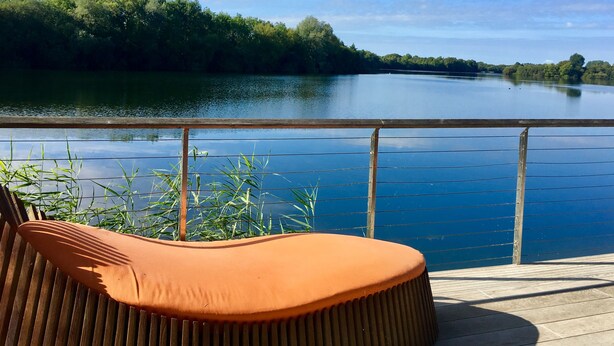 Een houten terras met een leuning, met uitzicht op een rustige rivier, omgeven door weelderige begroeiing.