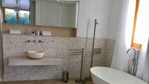 Een moderne badkamer met een vrijstaand bad, een backsplash van stenen mozaïek en een grote spiegel boven de wastafel.