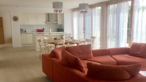 Een moderne woonkamer met een rode bank, een eethoek met een tafel en stoelen, en een keuken op de achtergrond.