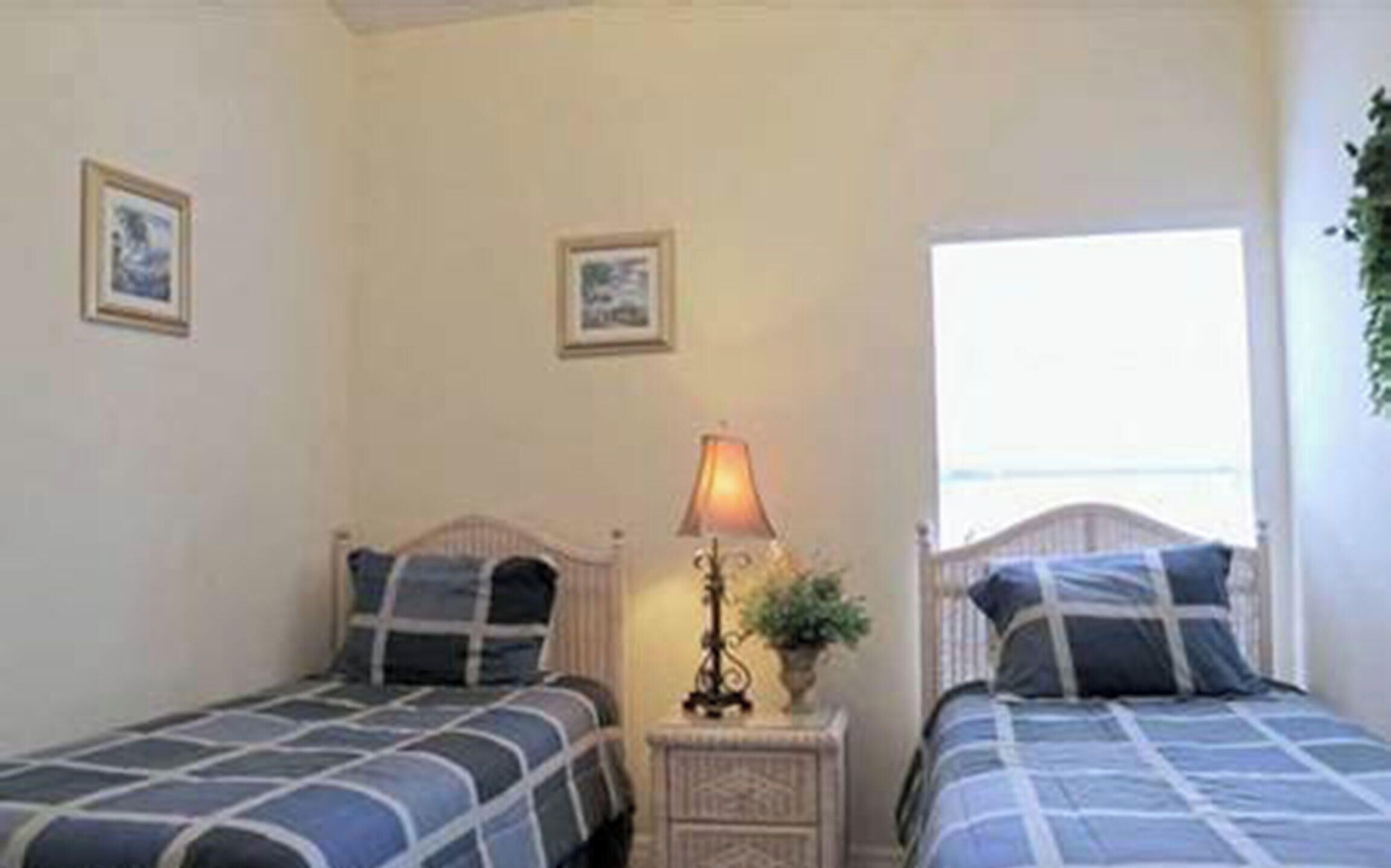 A room with two beds, a nightstand with a lamp, and a window.