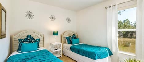 Un dormitorio con dos camas, una mesita de noche, una lámpara y un ventanal con cortinas.