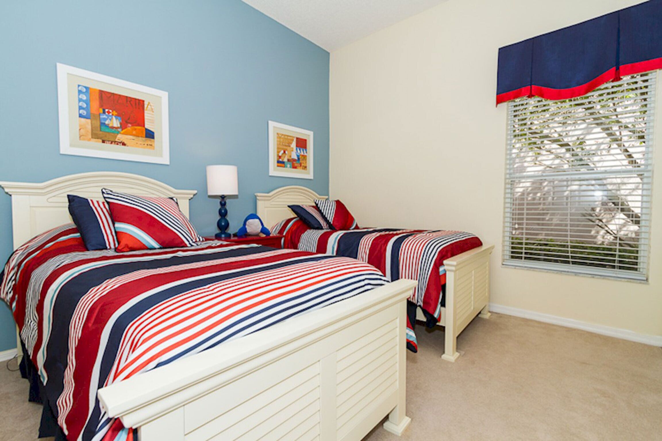 A bedroom with two beds, a window with blinds, and two framed pictures on the wall.