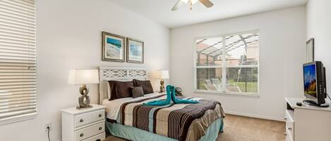 A bedroom with a bed, bedside tables, a ceiling fan, a TV, and a window with blinds.