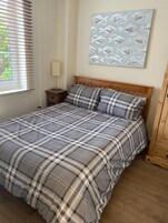 Un dormitorio con cama, mesita de noche, lámpara y una obra de arte en la pared.