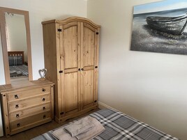 Un dormitorio con un armario de madera, un tocador, una cama con edredón escocés, un espejo y una pintura marina.
