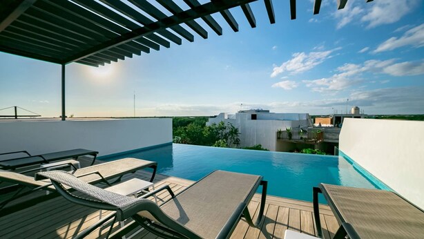 Uma piscina infinita ao ar livre com espreguiçadeiras e um pérgola, com vista para a paisagem urbana.