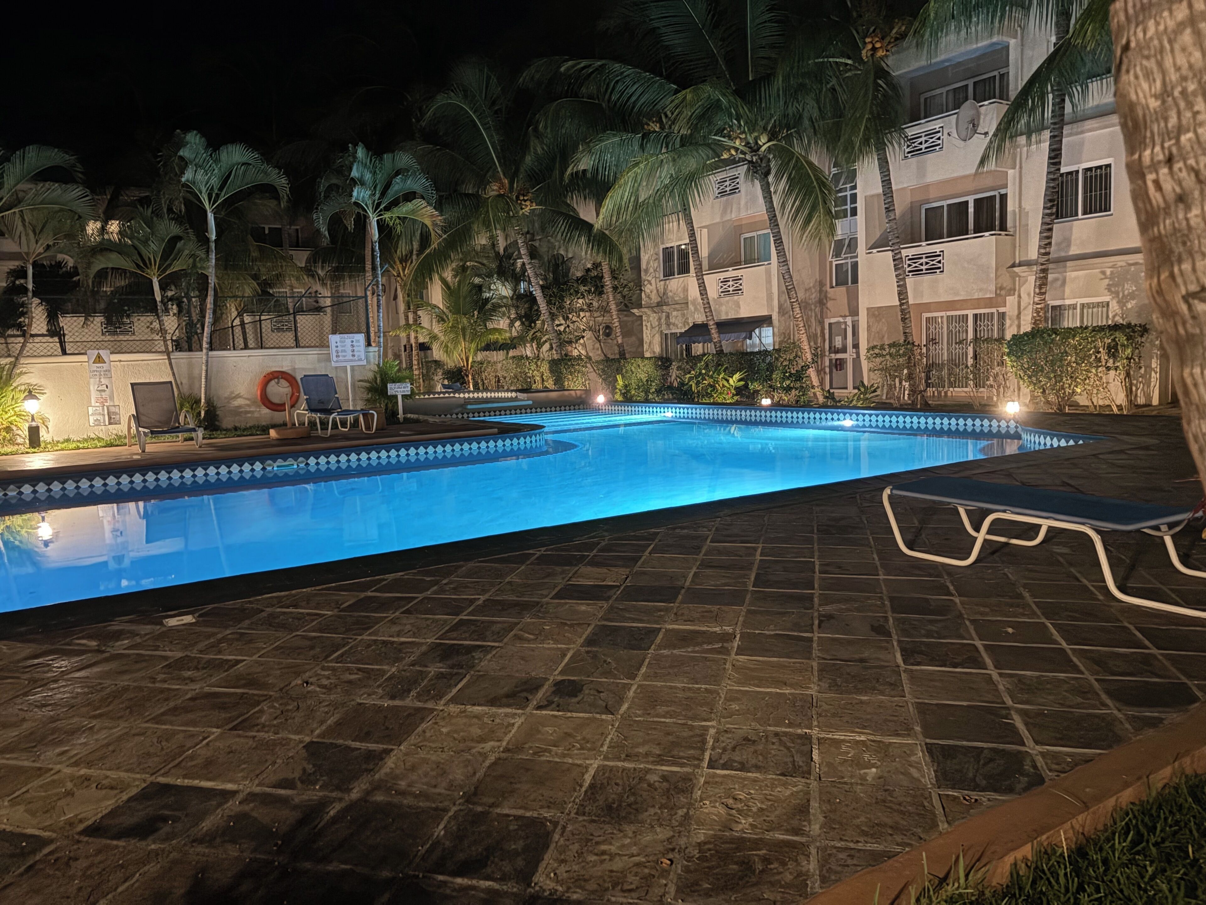 A swimming pool with lounge chairs, palm trees, and a building with balconies.