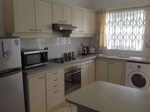 A kitchen with white cabinets, a microwave, stove, oven, sink, and a washing machine.