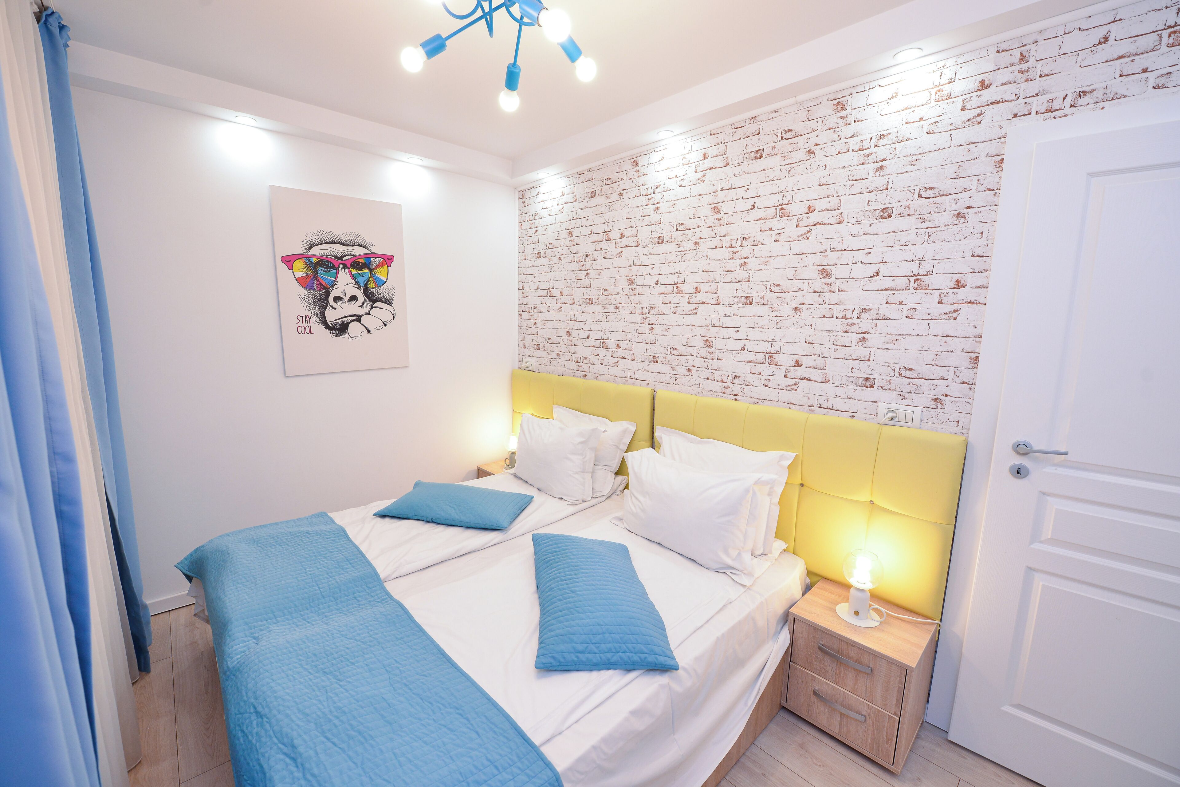 Une chambre à coucher avec un lit double, une table de chevet avec une lampe, un mur décoré d’un motif en briques et une porte.